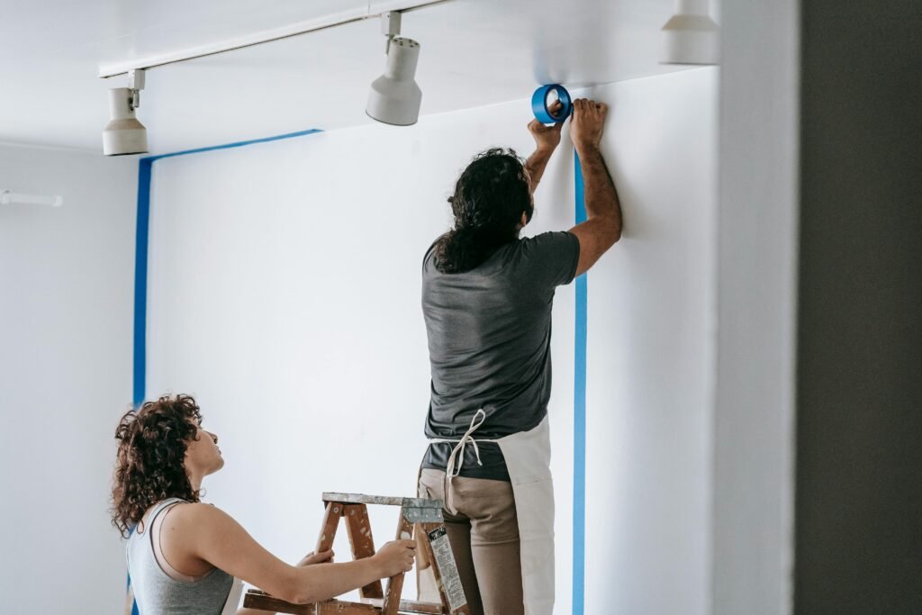 A man and woman working together on home renovation, applying painter's tape.